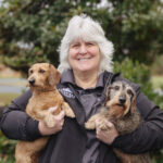 Deb smiling with two small dogs in hand